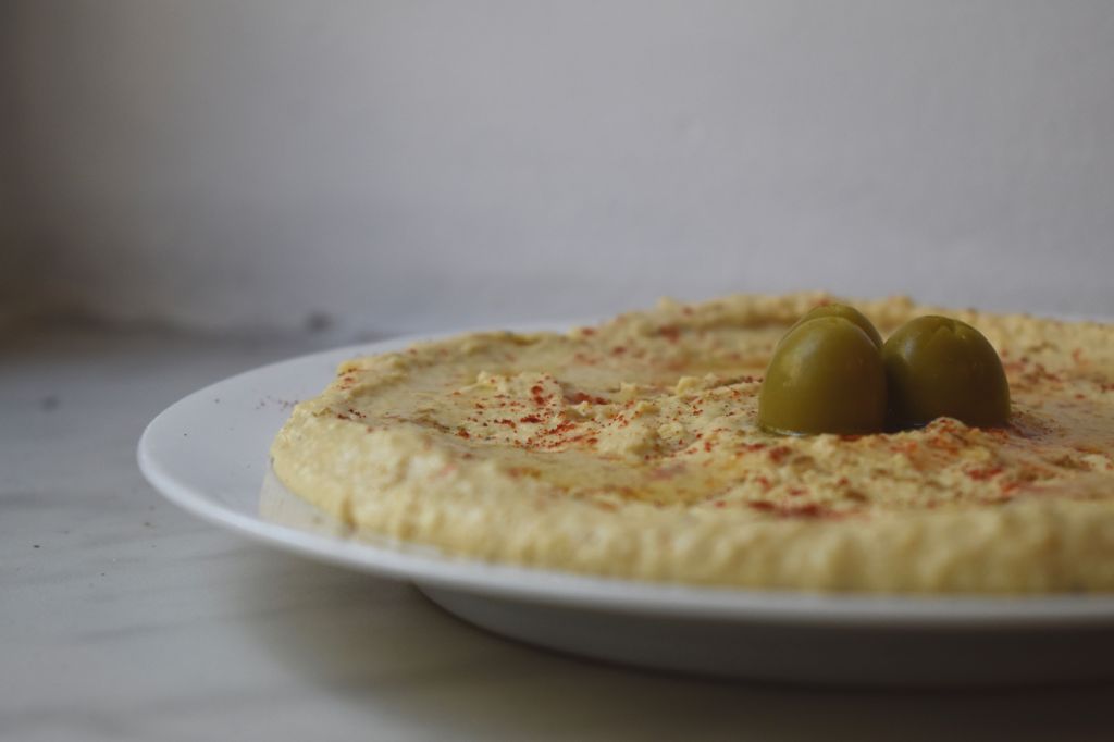 Hummus with olives and paprika on a white plate 